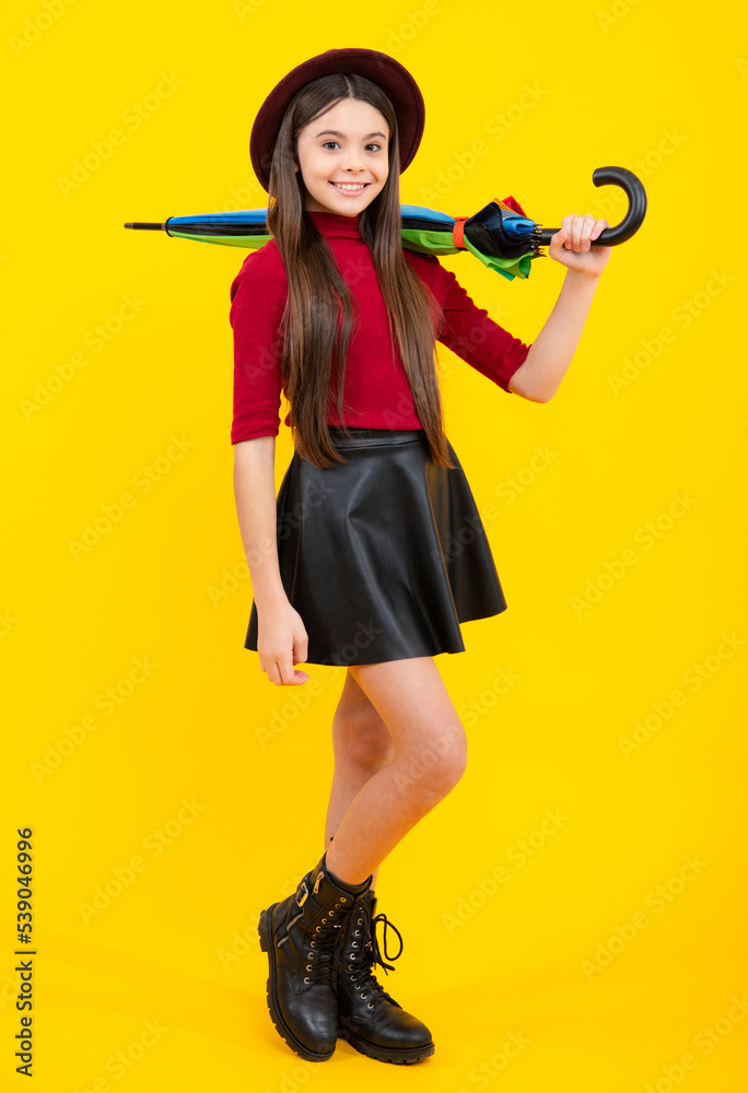 Autumn kids weather, full length. Child teenager girl with umbrella in autumn skirt, sweater, boots and hat isolated on yellow studio background. Autumn trendy clothes. Autumn kids weather, full length. Child teenager girl with umbrella in autumn skirt, sweater, boots and hat isolated on yellow studio background. Autumn trendy clothes.