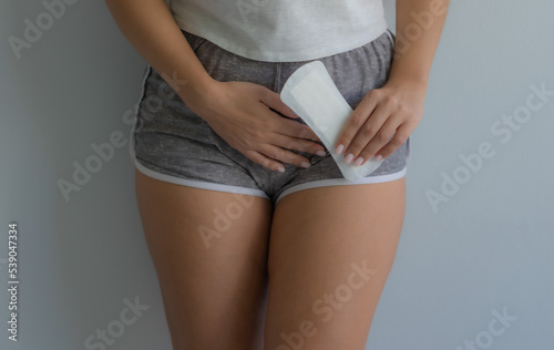 The girl holds her stomach with one hand. Holds a sanitary pad in the other hand. Menstrual pain. Women's health. Soft focus photo