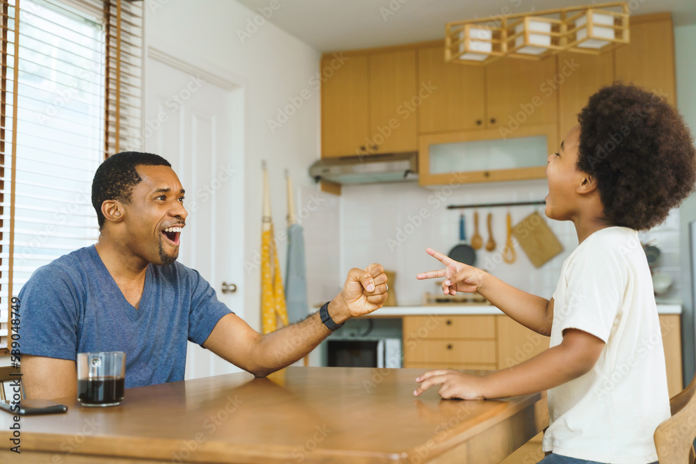 Cheerful Black African American father and little afro son playing rock scissors paper game at home together. Cheerful Black African American father and little afro son playing rock scissors paper game at home together.