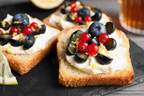 Tasty sandwiches with cream cheese  blueberries  red currants and lemon zest on slate plate  closeup