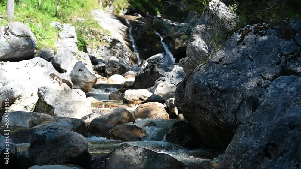 A mountain stream with rocks and a waterfall in the background (slow motion) A mountain stream with rocks and a waterfall in the background (slow motion)