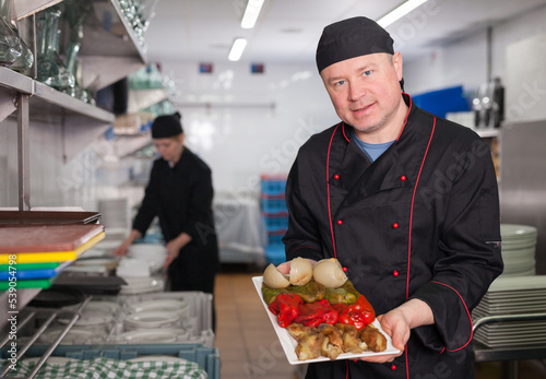 Skilled cook offering to taste just prepared appetizing dish in restaurant kitchen..