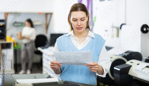 Woman looking at piece paper while working in printing office.