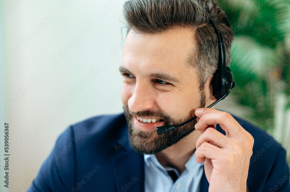 Close-up photo of a positive caucasian man with headset, call center worker, expert, company representative, support service operator, holds online consultation with client, looks to the side, smiling Close-up photo of a positive caucasian man with headset, call center worker, expert, company representative, support service operator, holds online consultation with client, looks to the side, smiling