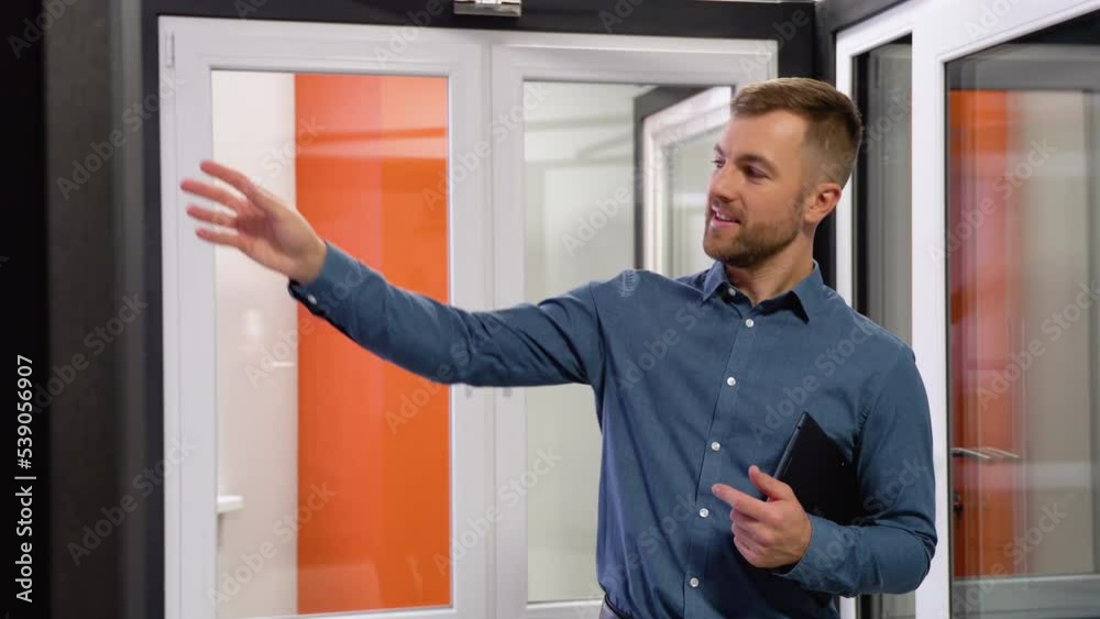 Friendly manager in window shop makes a presentation of new products. A large selection of windows and doors for the house Friendly manager in window shop makes a presentation of new products. A large selection of windows and doors for the house
