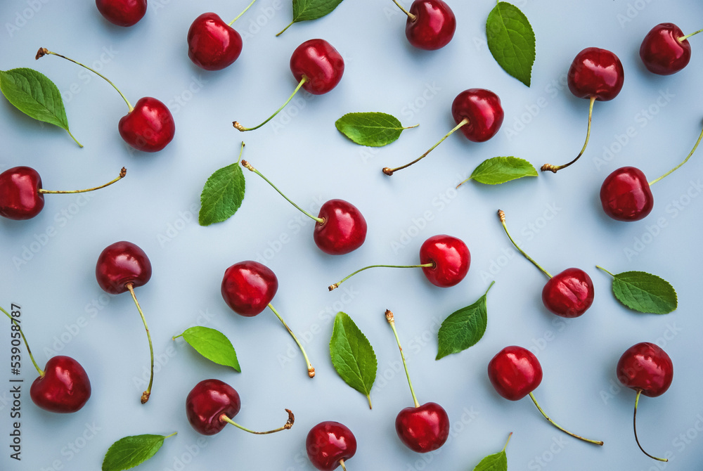 Red cherries and green leaves pattern on gray background, sweet cherry fruit pattern, overhead flat lay Red cherries and green leaves pattern on gray background, sweet cherry fruit pattern, overhead flat lay