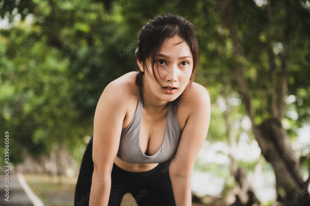 Asian woman wearing sportswear and tired engaged in fitness in public park. Her gaze was determined to lose weight. Healthy lifestyle activity concept Asian woman wearing sportswear and tired engaged in fitness in public park. Her gaze was determined to lose weight. Healthy lifestyle activity concept