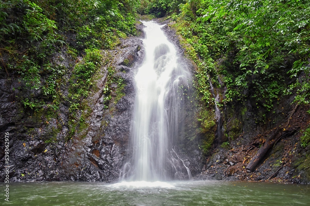 Waterfall Jaco Costa Rica, Catarastas Valle Encantado - Hidden waterfall surrounded by green trees, vegetation, rocks, leaves floating on green and clear water. Central America.