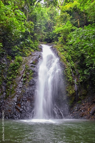 Waterfall Jaco Costa Rica, Catarastas Valle Encantado - Hidden waterfall surrounded by green trees, vegetation, rocks, leaves floating on green and clear water. Central America.