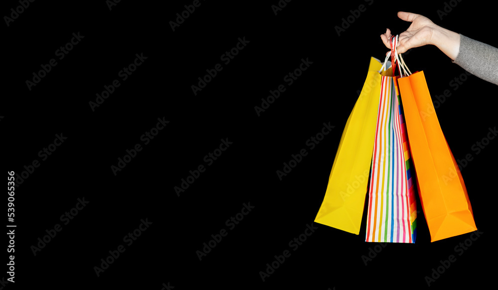 Close-up of a woman's hand holding colorful shopping bags over black background. Copy space. Shopping Concept