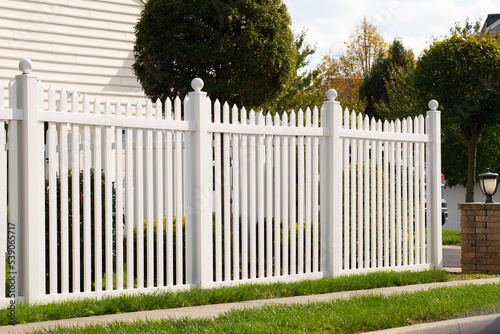 A new white vinyl fence by a grass area with trees behind it