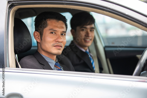 Two business men are driving and looking out of the car window.