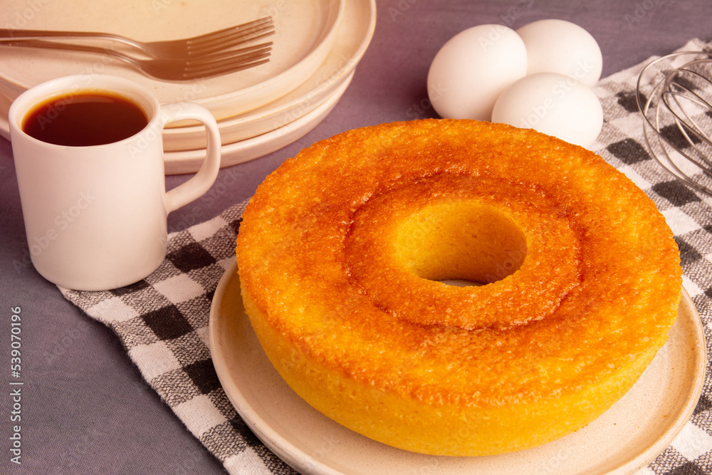 Homemade Redondo Pamonha Cake (Fuba Cake), made from corn, with a coffee and eggs in the background, on a checkered picnic tablecloth Homemade Redondo Pamonha Cake (Fuba Cake), made from corn, with a coffee and eggs in the background, on a checkered picnic tablecloth