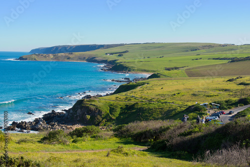 a far view of tourists and vehicles along the coast of victor harbor in summer of South Australia with crystal blue water and green landscape