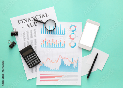 Business charts, mobile phone and stationery on green background