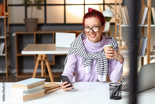 Young female student with phone and coffee preparing for exam at home