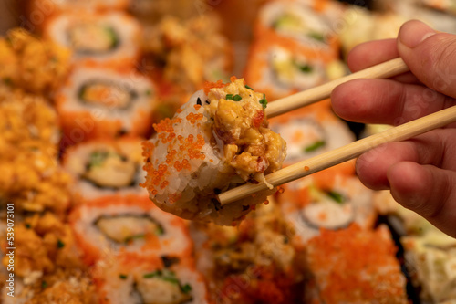 Someone takes a chopsticks roll from a set of different types of rolls in a box.