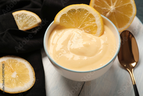 Wooden board with bowl of tasty vanilla pudding and lemon, closeup