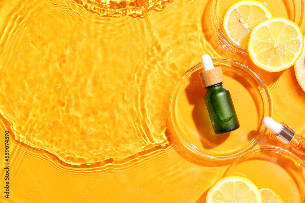 Bottle of vitamin C serum and lemon slices in water on color background - obrazy, fototapety, plakaty 