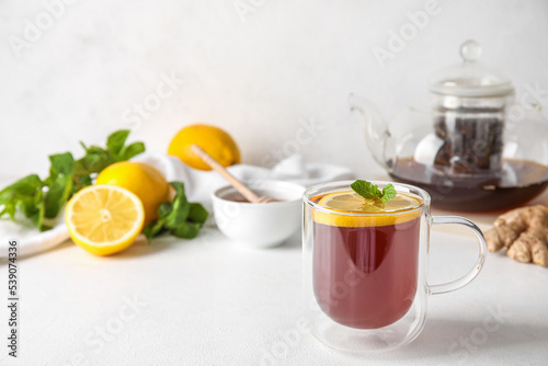Glass cup of black tea with lemon and mint on white table, closeup