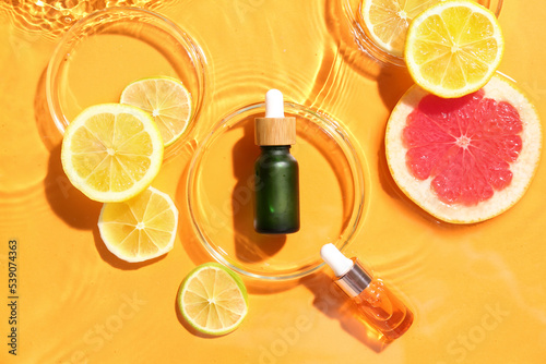 Fototapeta Naklejka Na Ścianę i Meble -  Bottles of vitamin C serum and fruits in water on color background