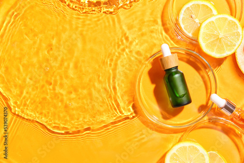 Bottle of vitamin C serum and lemon slices in water on color background photo