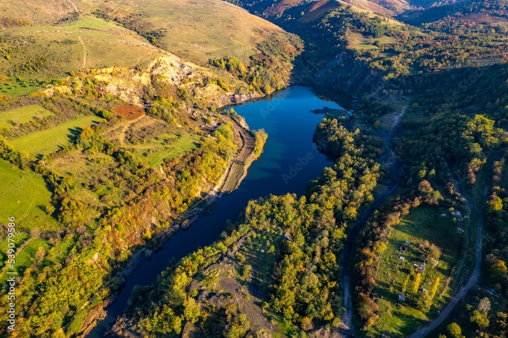 Obraz premium Aerial view of a small lake at sunset, that formed in a former coal mine exploitation, near Resita city, Romania. Captured with a drone, from above, in autumn setting. 