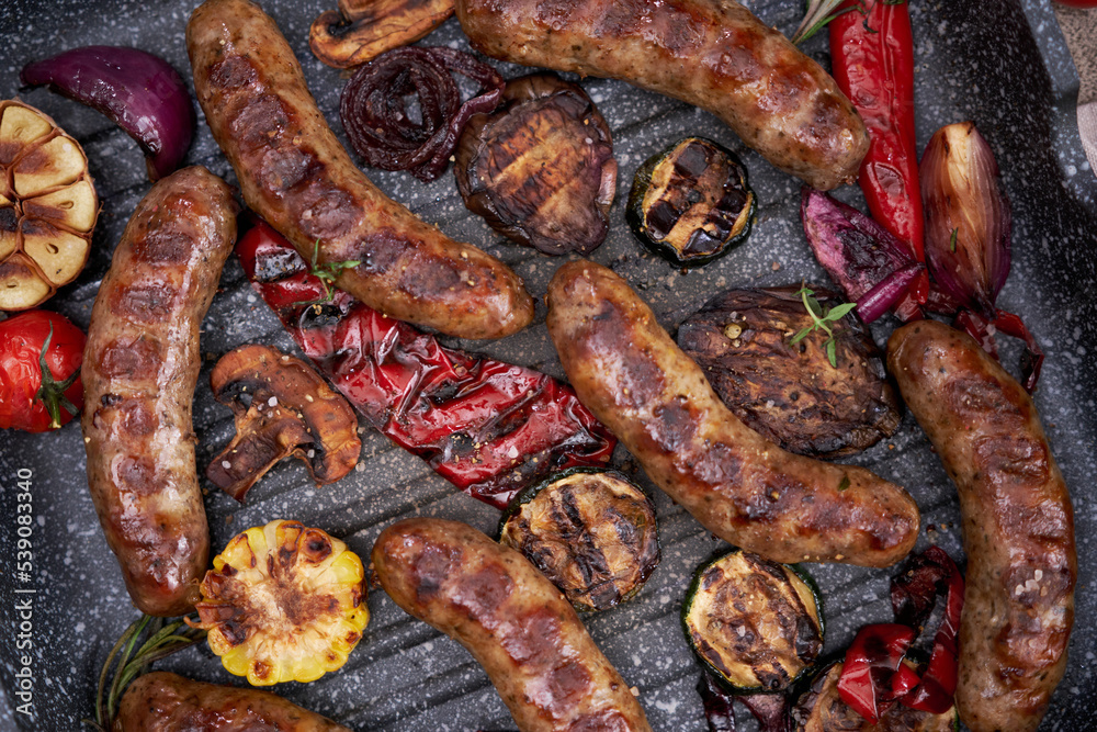 Fototapeta premium Grilled sausages and vegetables on a grill frying pan on a domestic kitchen