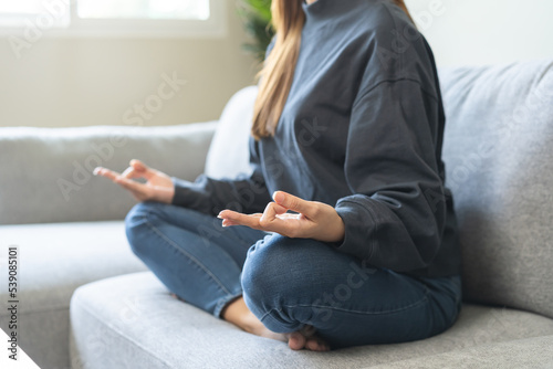 Beautiful asian young woman  girl hands in calm pose sitting practice meditating in lotus position on sofa at home  meditation  exercise for wellbeing  healthy care. Relaxation  happy leisure people.