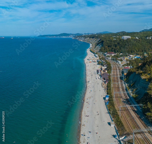 long Black Sea pebble beach with clear water on a windless sunny summer morning - aerial drone view of the horizon towards the city of Tuapse