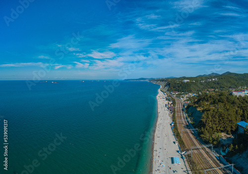 long Black Sea pebble beach with clear water on a windless sunny summer morning - aerial drone view of the horizon towards the city of Tuapse