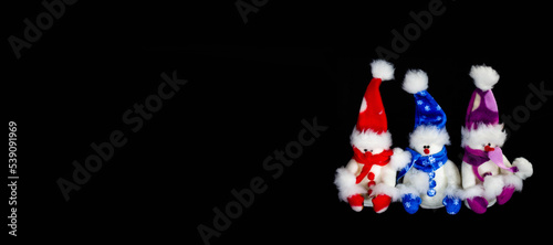 Banner with three handmade toy snowmen with hats and scarves on a black background. Christmas and New Year concept