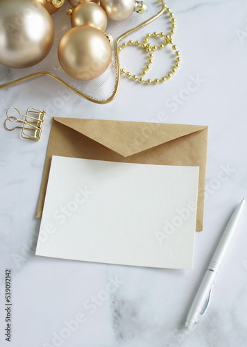 Blank greeting card, invitation mock up,craft envelope, Christmas tree gold  decorations top view on white marble desk with copy space.Xmas  scene still life .