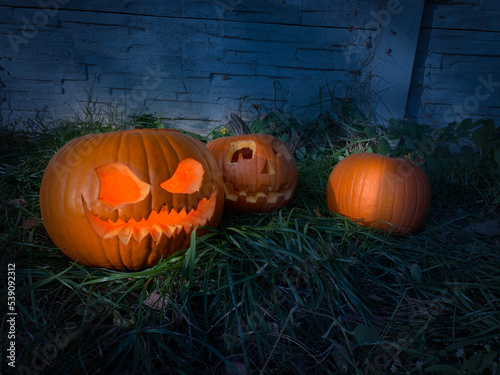 Dark Pumkin Jack O' Lantern with light inside in garden with pumpkins in the background. Autumn leaves on the ground. Grass, soil, fire