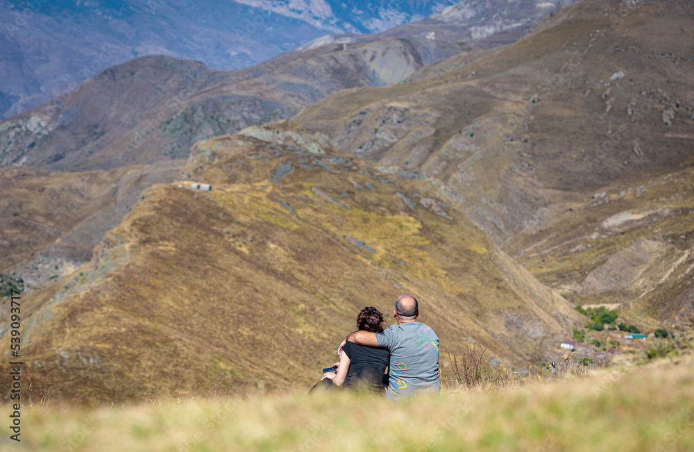 A man and a girl are sitting on a hill in the mountains. Happy couple. The man hugs the girl. Caucasus mountains, Ossetia.