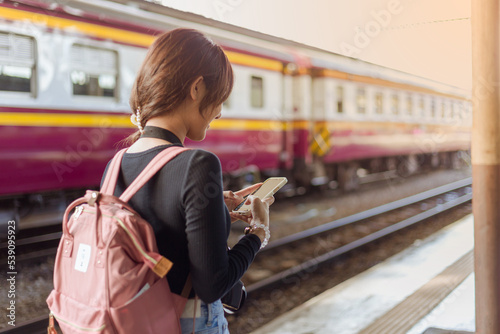 woman wearing black long sleeve t-shirt carrying backpack on shouder holding cellphone standing in railway station,travel concept,social network technology concept