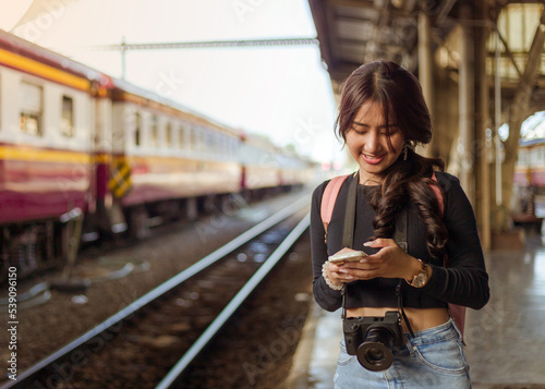 back view of woman wearing black long sleeve t-shirt carrying backpack on shouder holding cellphone standing in railway station,travel concept,social network technology concept © pichet