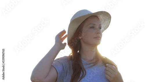 a red-haired woman in a straw hat against a blue sky in a field at sunset