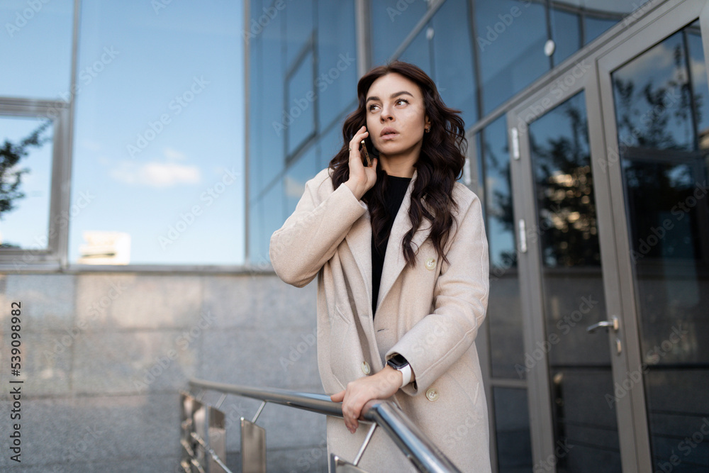 stylish businesswoman talking on a mobile phone at the entrance to the office center