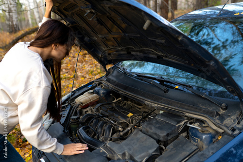 a woman peeks under the hood. a woman repairs a car. car breakdown