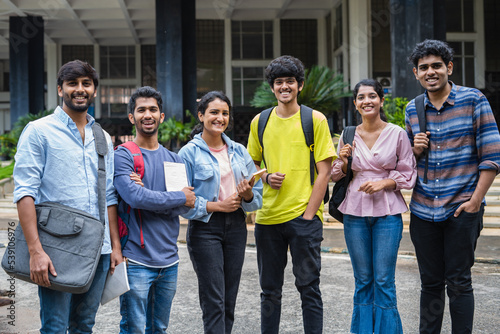 Group of happy students standing with books and backback by looking camera at college campus - concept of friendship, togetherness and education.