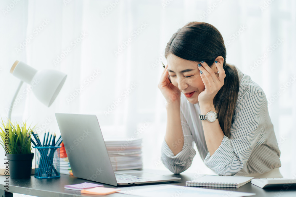 Young Asian woman feeling migraine head strain. Tired, Overworked businesswoman financier while working on laptop computer in office. Young Asian woman feeling migraine head strain. Tired, Overworked businesswoman financier while working on laptop computer in office.