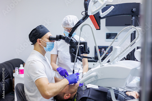 Dentist and assistant check patient's teeth with dental tools - microscope, mirror and probe in dental clinic office. Concept of medicine, dentistry and healthcare. Dental equipment