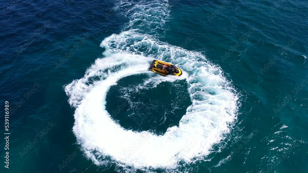 Aerial drone top down video of jet ski watercraft performing circles showing off in high speed operated by stuntman in deep blue sea