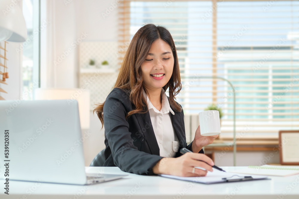 Professional businesswoman sitting front of laptop and checking information on notebook. Professional businesswoman sitting front of laptop and checking information on notebook.