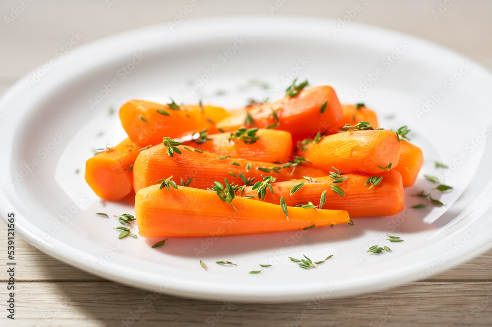Baked (roasted) honey glazed baby carrots with thyme on a ceramic plate. Baked (roasted) honey glazed baby carrots with thyme on a ceramic plate.