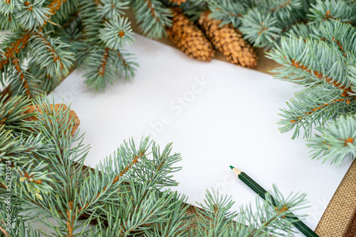 christmas frame with fir branches and cones, on white writing paper and green pencil