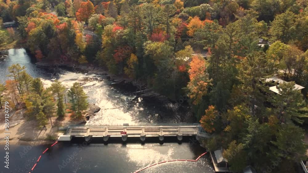 Beautiful landscape view, aerial flyover Port Sydney Falls, capturing golden sunlight reflection on the water surrounded by vibrant and colorful tree foliages in autumn at Huntsville, Ontario Canada. Beautiful landscape view, aerial flyover Port Sydney Falls, capturing golden sunlight reflection on the water surrounded by vibrant and colorful tree foliages in autumn at Huntsville, Ontario Canada.