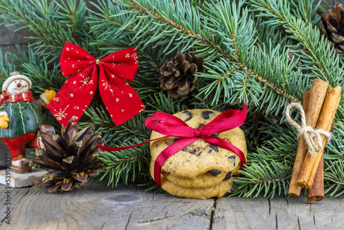 Christmas (New Year) decoration composition. Chocolate chip cookies decorated red bow, cinnamon sticks, toy snowman fur-tree branches and cones on wooden background