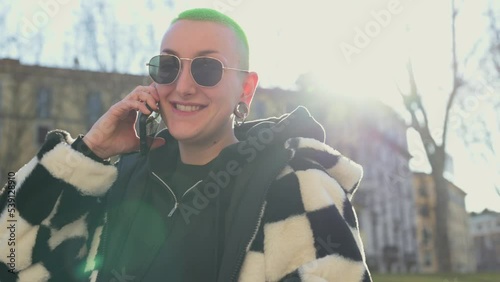 Curvy young androgynous having a phone call with friends, female person using smart phone outdoor
